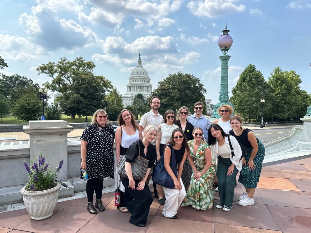 CSPI interns and staff pose with the U.S. Capitol building in the background on a sunny day with scattered clouds.