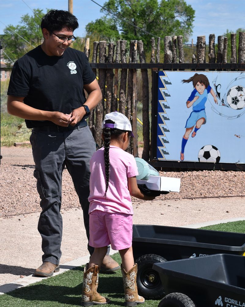 Picture of a young man standing over a little girl as she loads items into a small cart.
