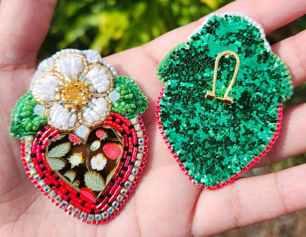 The same pair of earrings but with one flipped over to show the backing. The backing is glittery green with golden fingernail posts. 