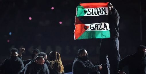 Dancers in Black and one is on top a car holding a flag of Palestine and sudan