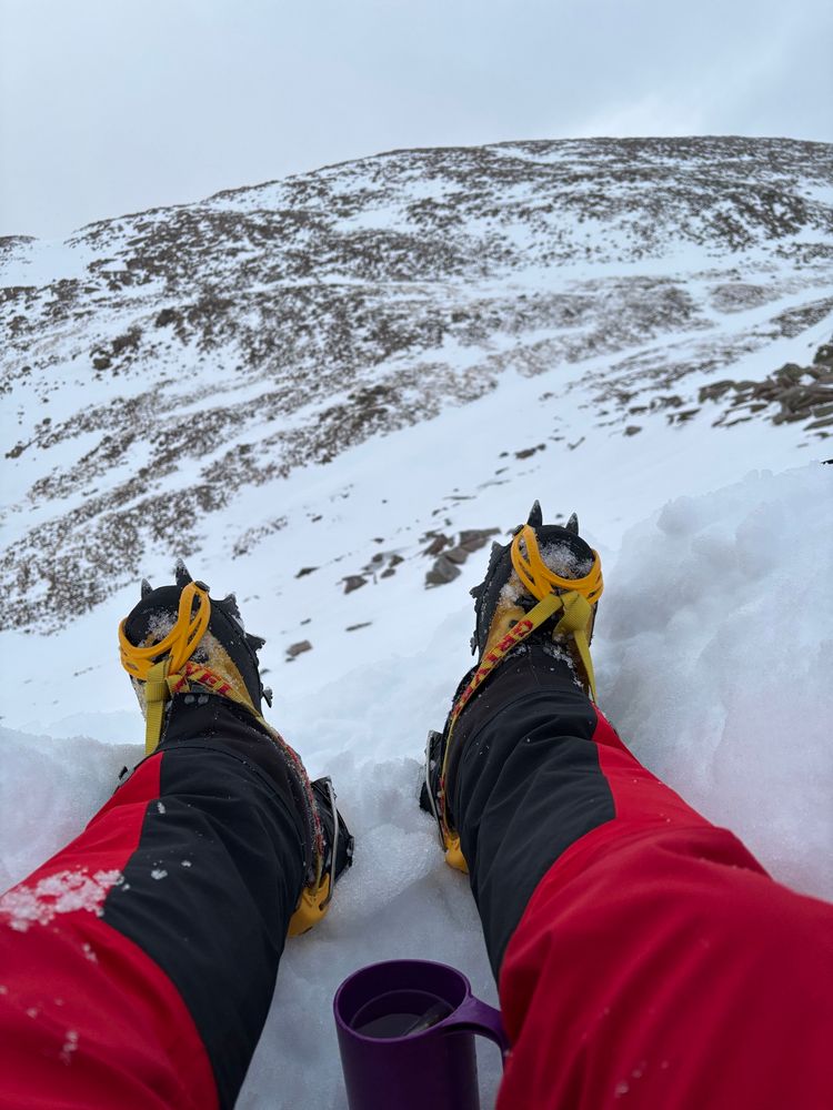 Looking at legs with crampons on. A snowy slope beyond 