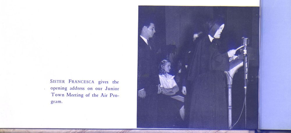Black and white photo of a Sister of Charity in habit standing in front of an old-fashioned microphone and reading from a note in her hand. A young man in a suit and tie stands behind her, and a young woman with 40's-style hair, blouse, and skirt is seated beside him. 