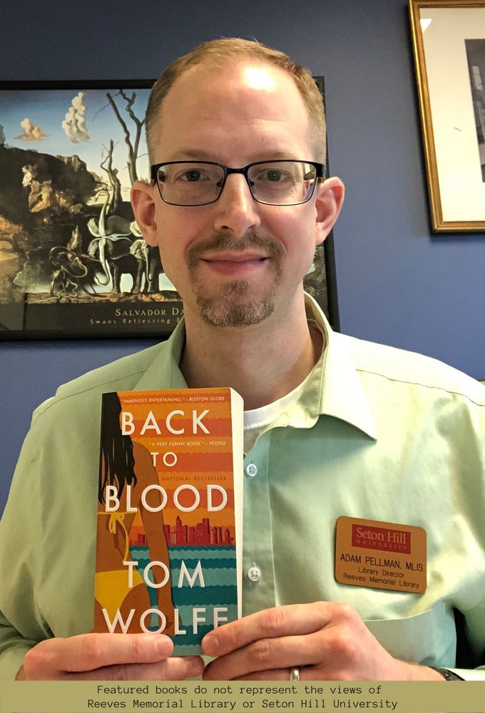 Adam holding a paperback copy of Back to Blood by Tom Wolfe