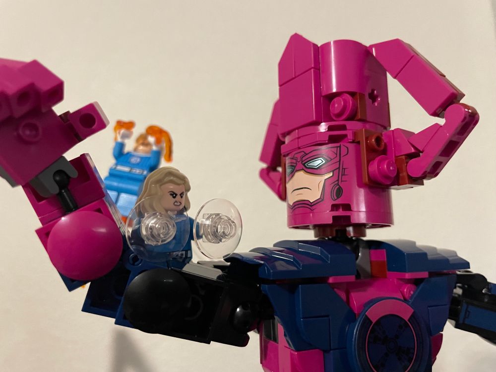 Galactus back hands the Human Torch as an enraged Invisible Woman tries to keep hood of Galactus’ arm. 

Lego Marvel Set 76316: “Fantastic Four vs. Galactus Construction Figure”