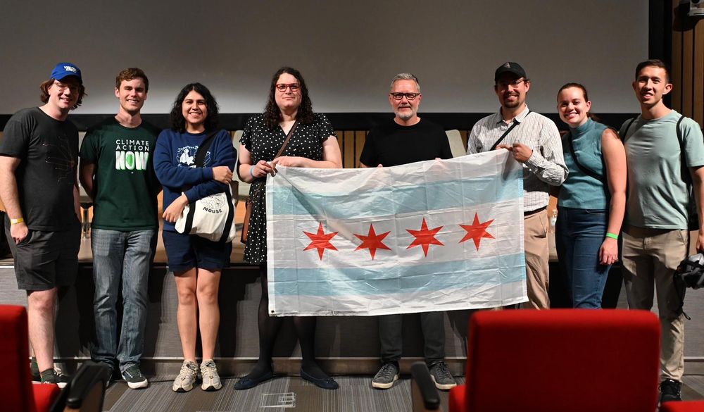 Several people standing around Ray Delahantey (AKA Citynerd), holding up a flag of Chicago. 