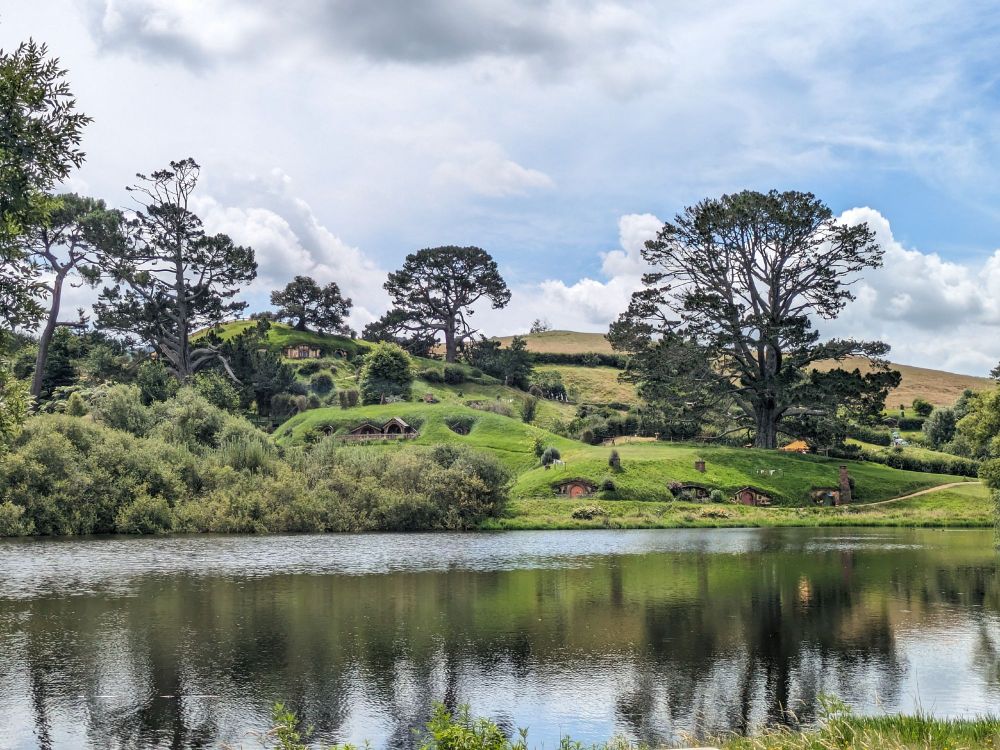 A lake in front of several Hobbit holes and the "party tree" in the Hobbiton movie set, Matamata.