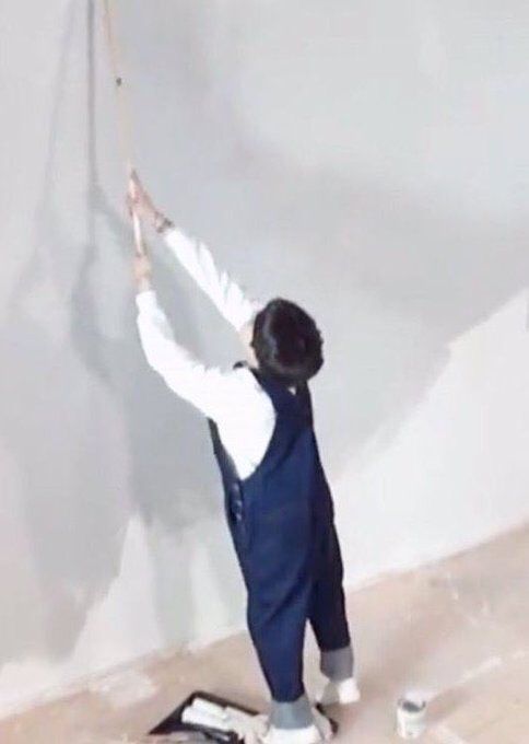 Yoongi is looking infinitesimally small on tippy toes in his denim onesie and white long sleeve and boba hair as he’s trying to paint the wall up high