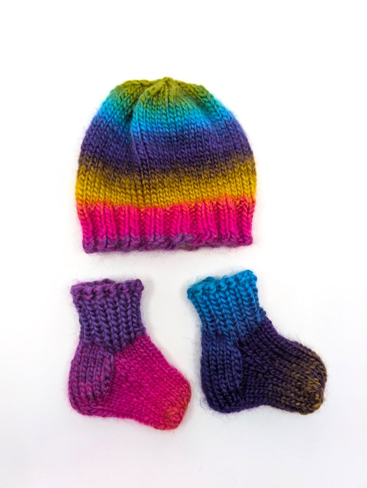 A knit newborn hat and booties made out of rainbow variegated yarn