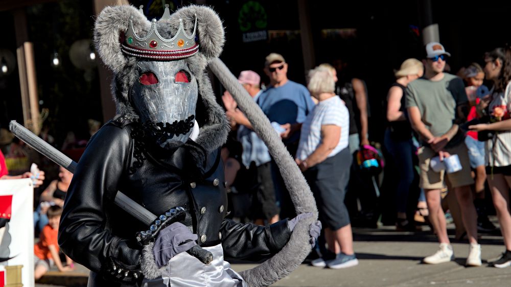 Photo of person wearing what is possibly some type of rat king costume, gray costume with gray crown, rat tail, leather jacket, sword, red eyes