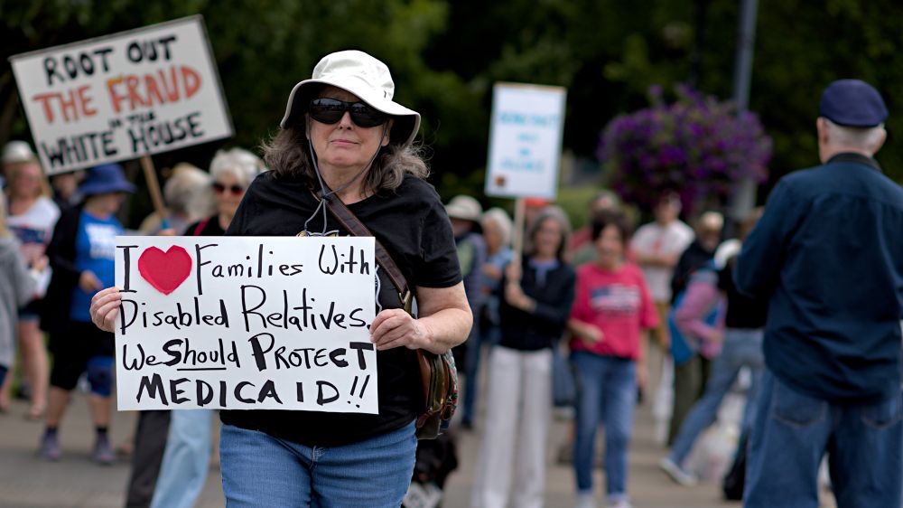 Olympia Washington, person holding protest sign, i heart families with disabled relatives we should protect Medicaid!!, other protesters seen in background