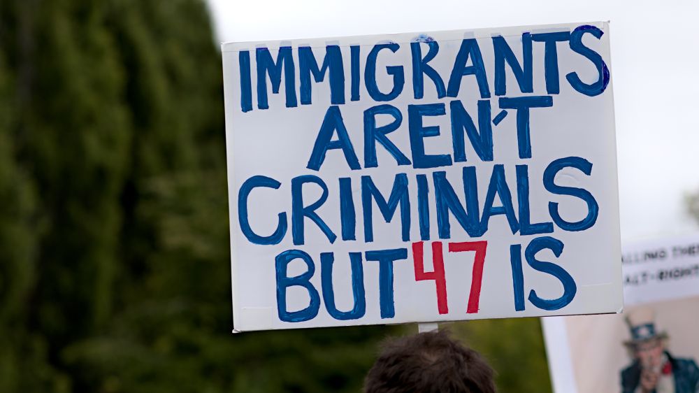 Olympia Washington, protest sign, blue text, Immigrants aren't criminals but 47 is, with 47 in red text