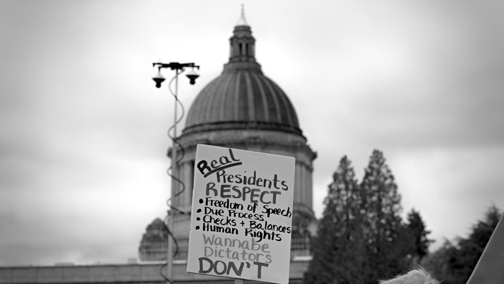Olympia Washington, monochrome photo, photo of protest sign with video surveillance system pole behind it, with capitol dome in background. Protest sign, Real presidents respect freedom of speech, due process, checks and balances, human rights, wannabe dictators don't