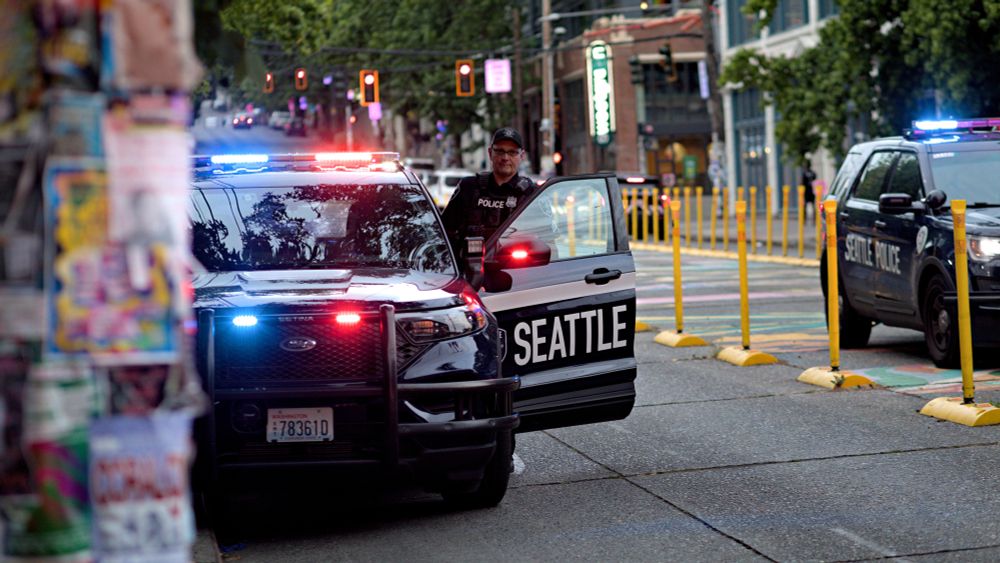 Photo of Seattle Police Department vehicle with SPD officer entering vehicle, additional SPD vehicle also seen.