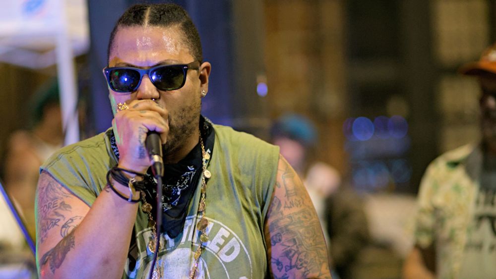 Closeup photo of person with sunglasses on singing, rapping into microphone