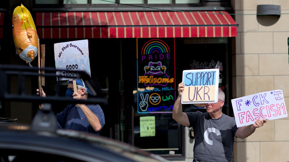 Two protesters on Broadway holding protest signs, Trump Baby balloon, we shall overcome good trouble, support UKR Ukraine, F*CK FASCISM, Trump's Asshole is Elon Musk! - Pride Capitol Hill sign in background