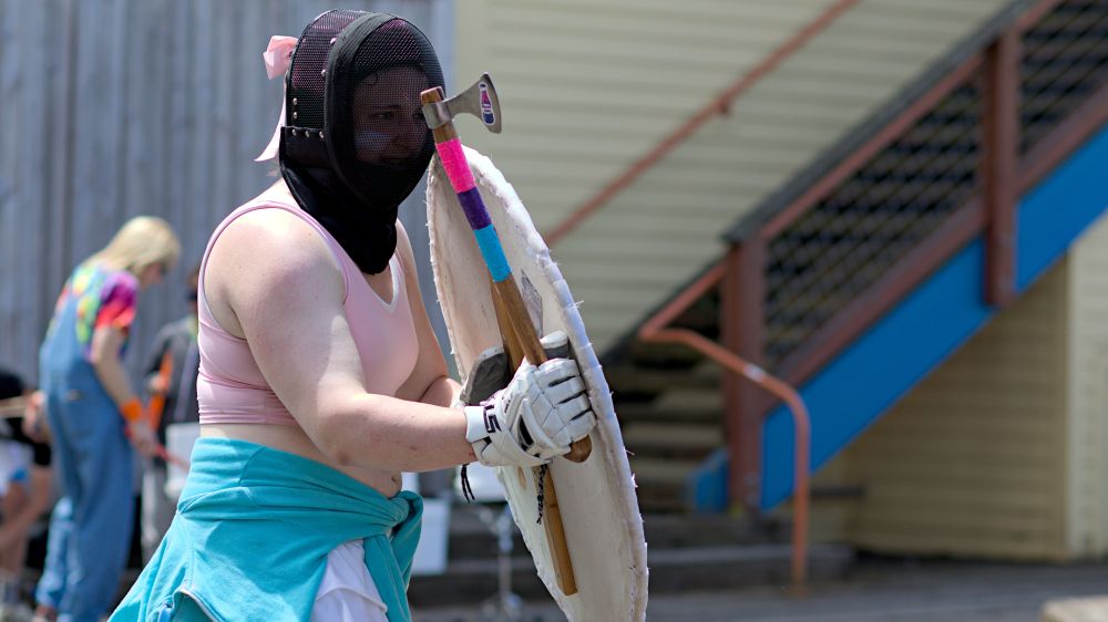 LARP live action role play participant with axe, shield, pride colors, fencing helmet