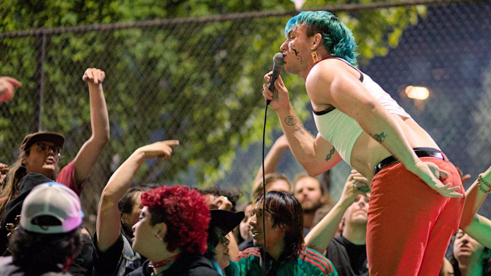 Photo of singer with microphone standing over crowd that is watching concert, many dancing, gesturing