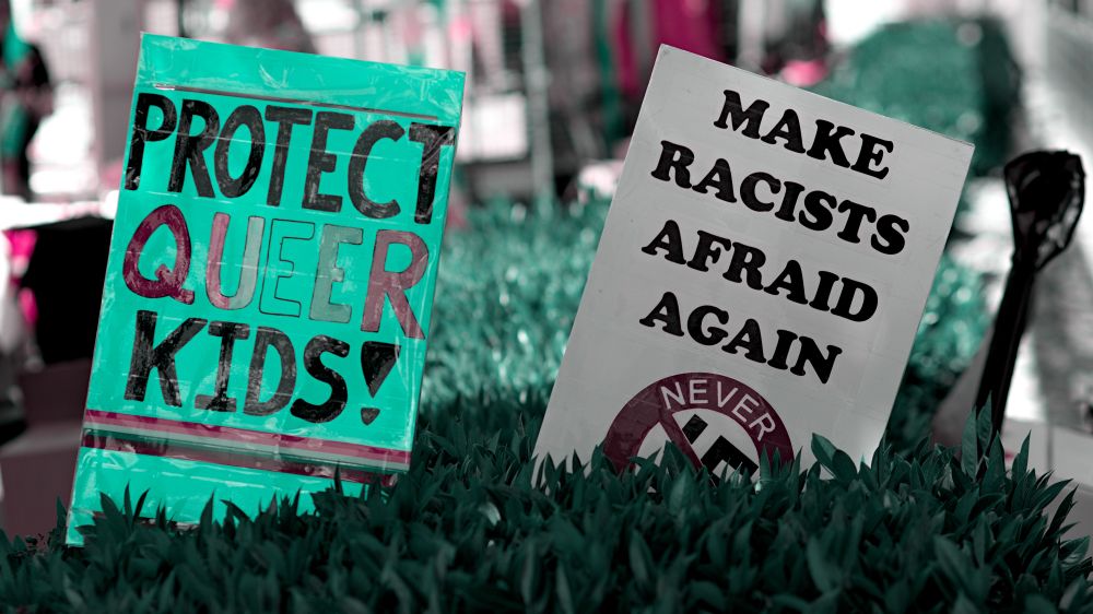 Two protest signs, protect queer kids! Make racists Afraid Again, never circled swastika with a slash through it