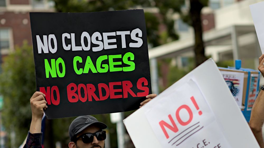 Photo of person holding protest sign, no closets no cages no borders