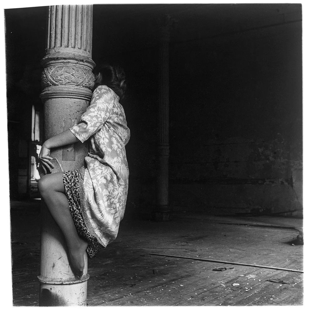 Black and white photo of a girl clinging to a streetlight pole. Face hidden
