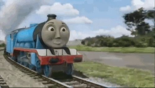 a thomas the tank engine train is going down the tracks in a field .