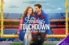 An alarmingly pretty couple sitting on the goal posts in Ralph Wilson Stadium )you heard me).  They are wearing Bills clothing and the goal posts are wrapped in Christmas lights. 