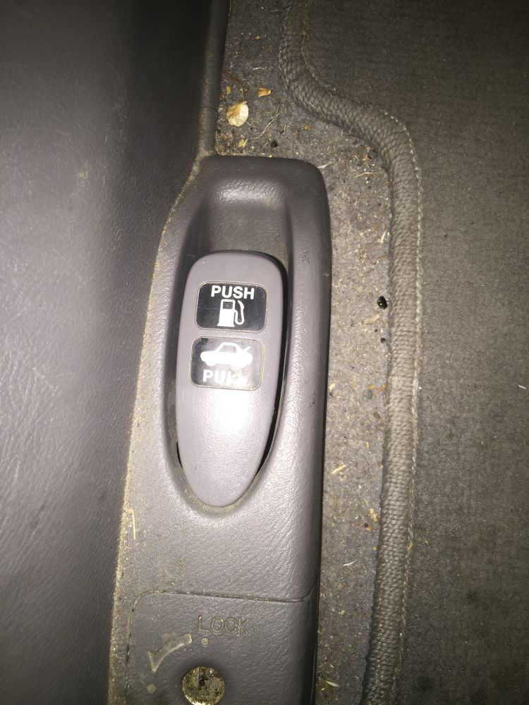 A dirty Honda civic floor with a the trunk/gas lever