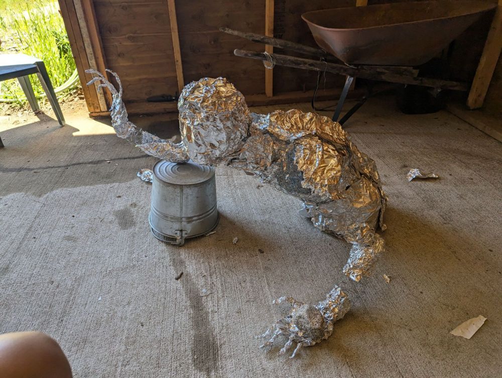 A figure made to look as if coming out of the ground made of tinfoil and chicken wire. (Left side view)
