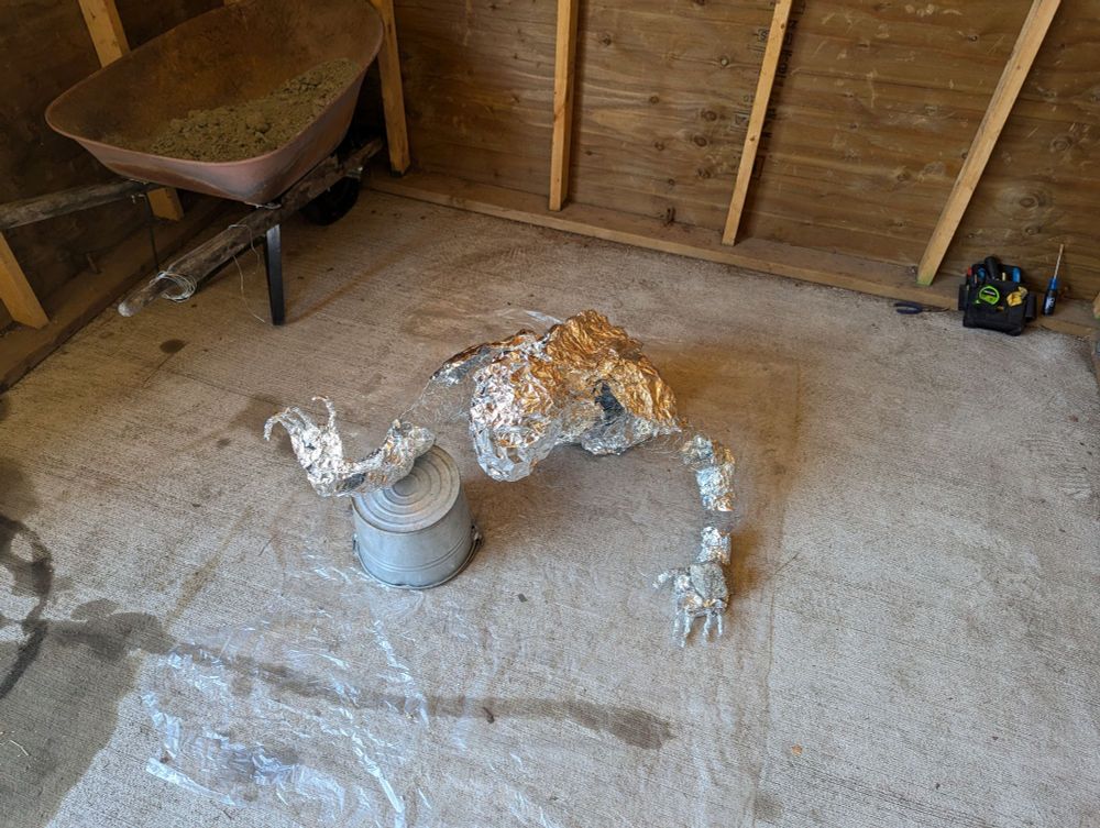 A figure made to look as if coming out of the ground made of tinfoil and chicken wire. (Left front view)