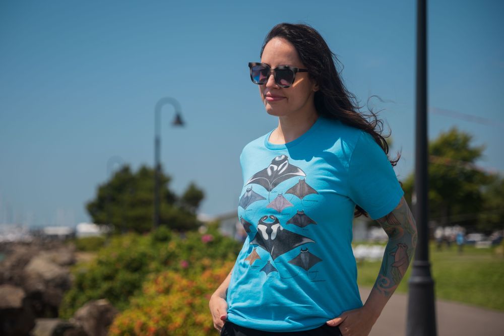 My BFF wearing a bright blue shirt with paintings of manta rays and devil rays on it. She's wearing sunglasses and clearly loves rays!