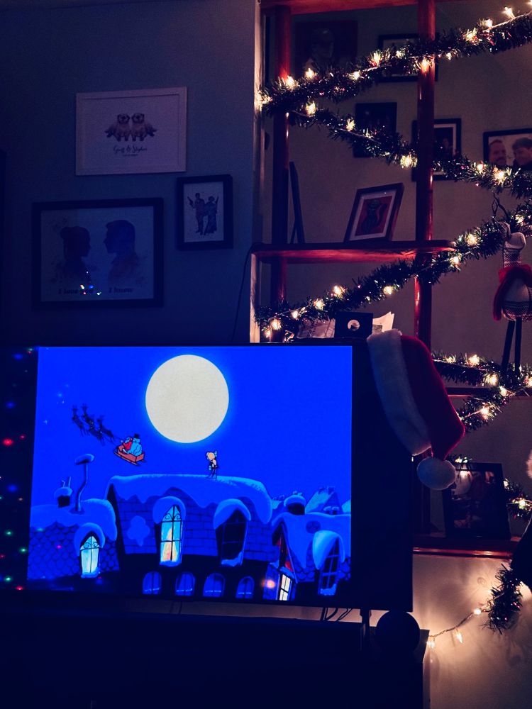 Image of the ending of Frosty the Snowman cartoon on the TV depicting a young girl on the roof and Santa Claus and Frosty flying away in Santa’s sleigh.