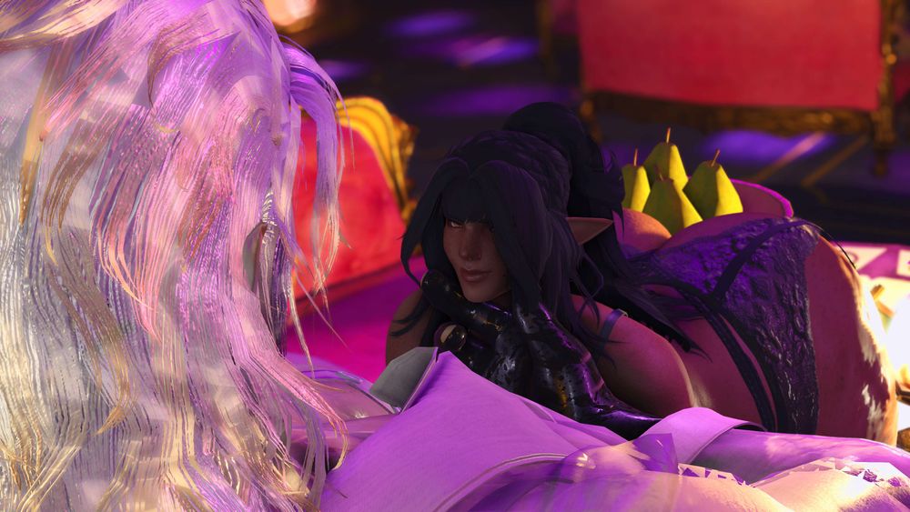 A view from over Mighty's shoulder. She is tenderly holding Maryam's chin with the index and thumb of her right hand, meeting her gaze. The dark-skinned woman smiles with charm.