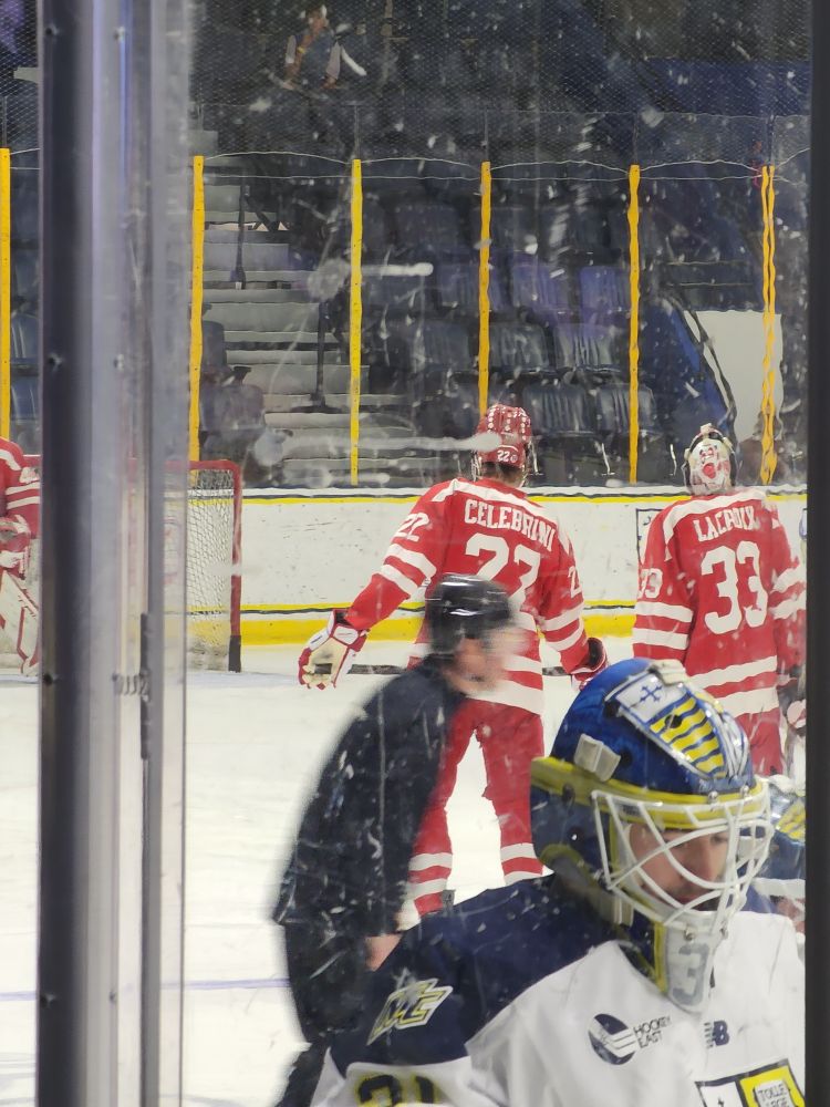 Picture of Aiden Celebrini (Boston University Terriers men's hockey) with blurry foreground of Merrimack College men's hockey Goaltender Keyes.