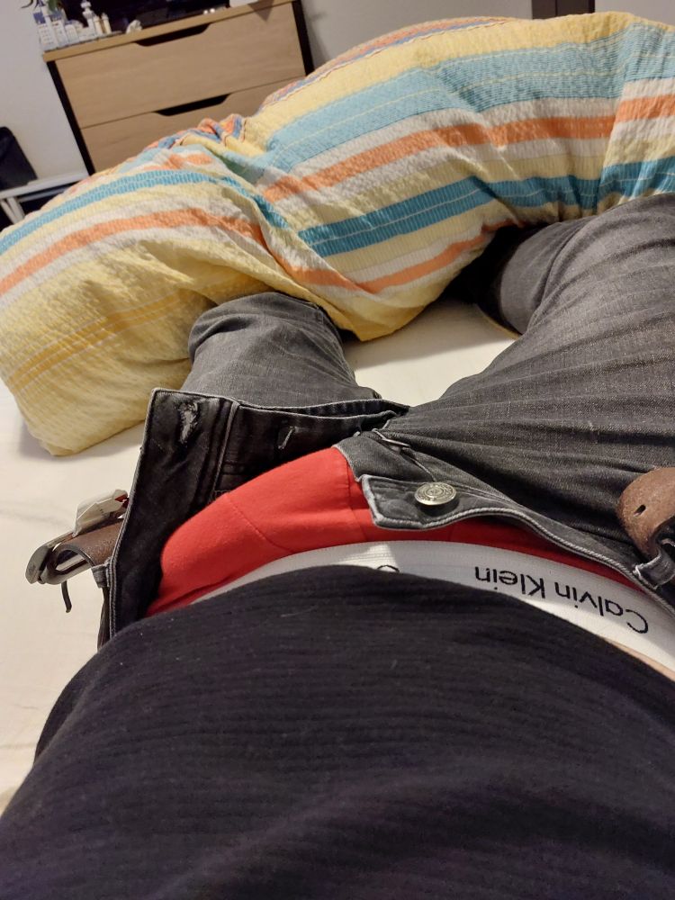 Ich liege bekleidet auf dem Bett, meine Jeans ist geöffnet und man sieht eine Beule in meiner roten CK Boxer