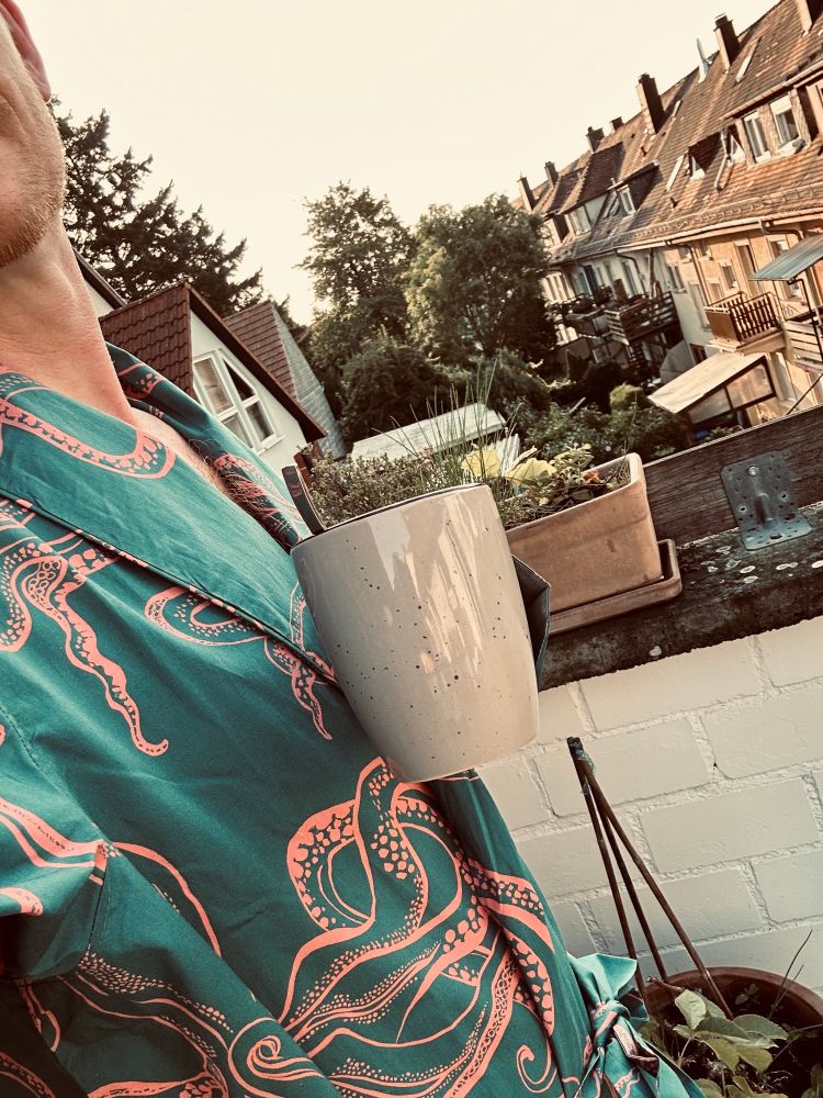 Ich, im Morgenmantel auf der Terrasse mit Kaffeetasse in der Hand.