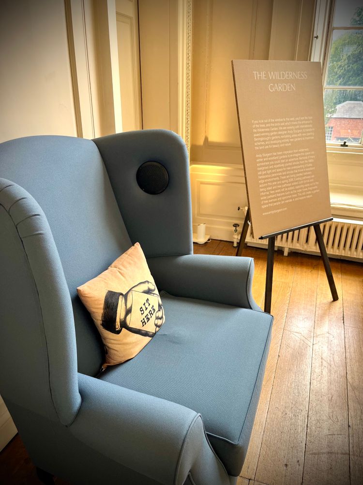 An audio chair, with a cushion labelled ‘sit here’ and a National Trust information placard next to it 