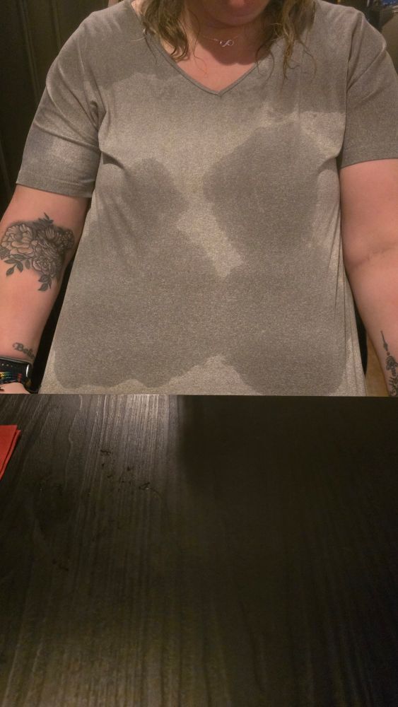 Person in a light grey t-shirt that is mainly dark grey because it is wet through from torrential rain.