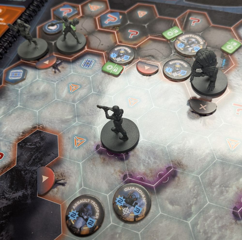 Mass Effect:The board game set up on a table, with various figures and chits on a book background
