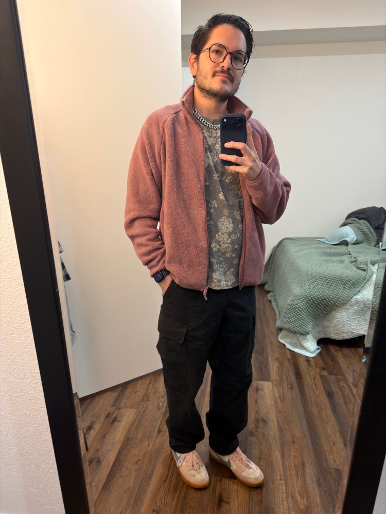 Pic of me standing in front of a mirror wearing black cargo pants, a floral shirt, and a pink fleece with pink Nike shoes 