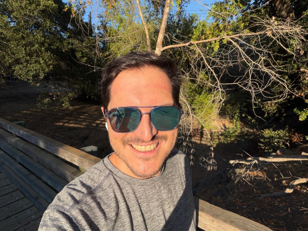 A photo of me on a wooden bridge facing the sun and wearing blue tinted sunglasses 