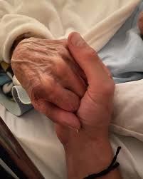 Dos manos agarradas. Una es de una persona joven. La otra, de una persona mayor aparentemente en la cama de un hospital.