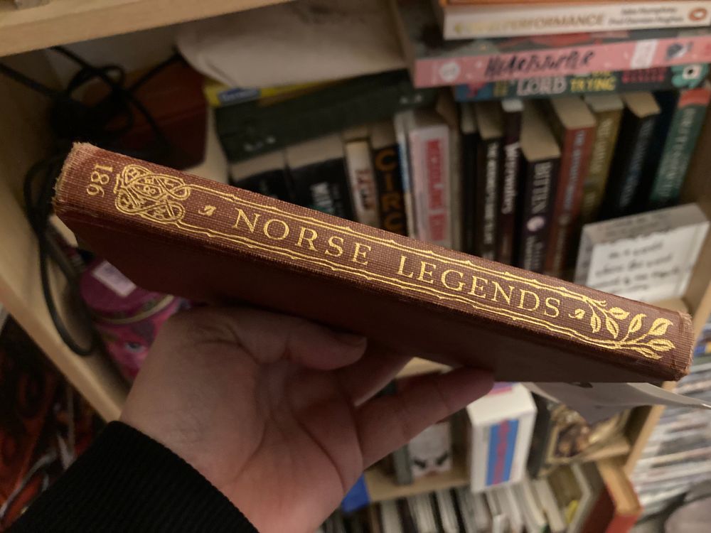 Spine of an old book. It’s a tan brown colour with gold lettering and decorative lines and leaves. The lettering says Norse legends