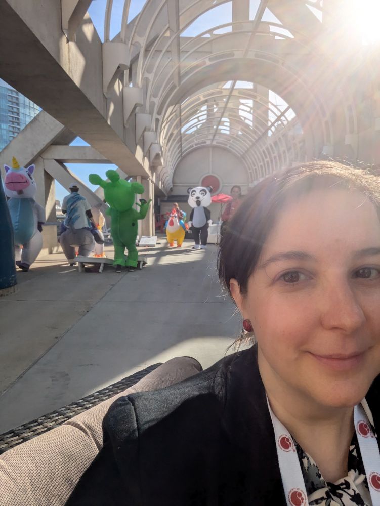 A selfie with costumed characters playing cornhole in the background.