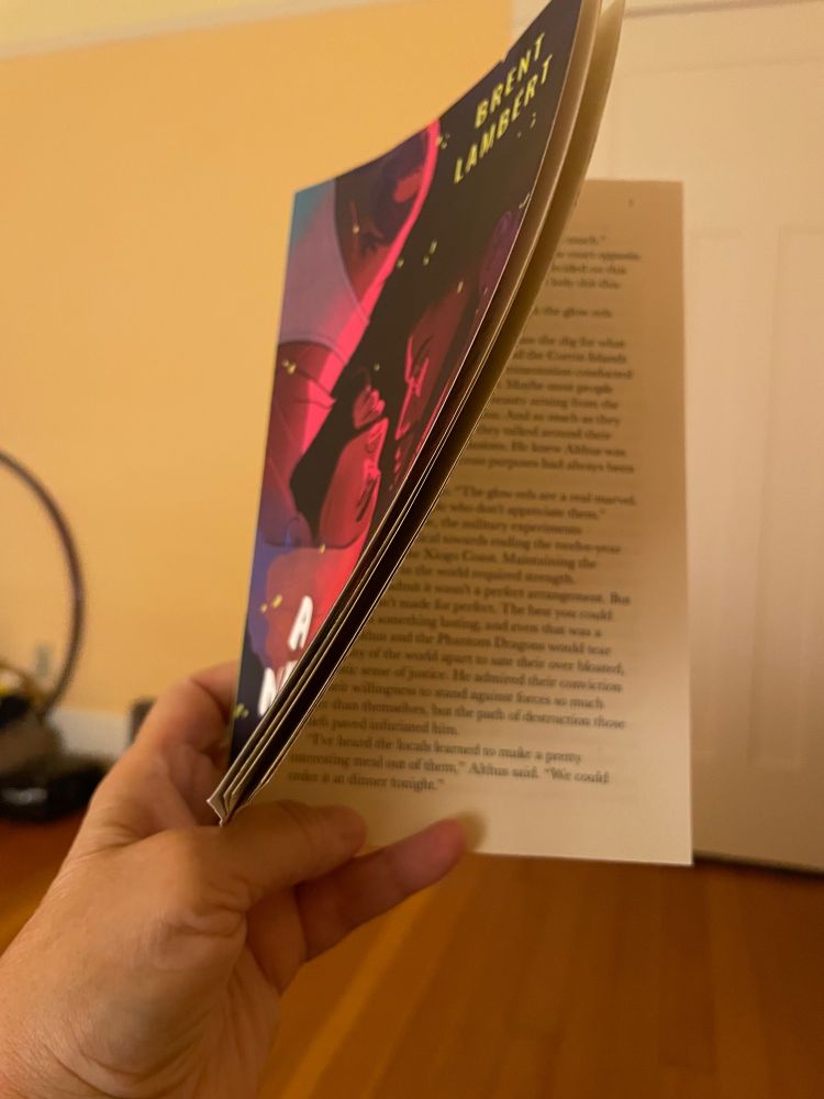 Hand holding open a book with a partial view of the cover of A Necessary Chaos, by Brent Lambert and a partial view of a page close to the beginning.