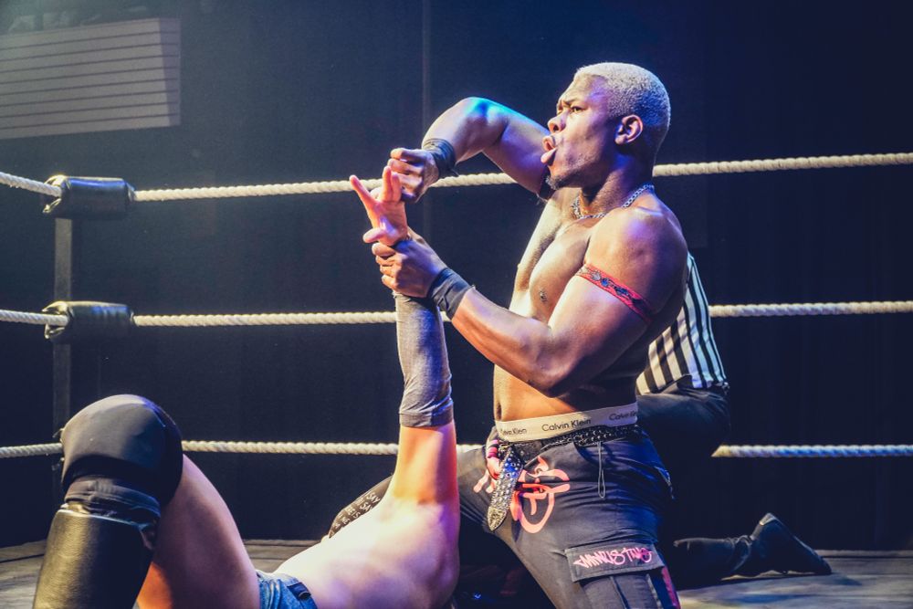 One wrestler has taken his opponent onto the mat and is now immobilising him, bending his fingers