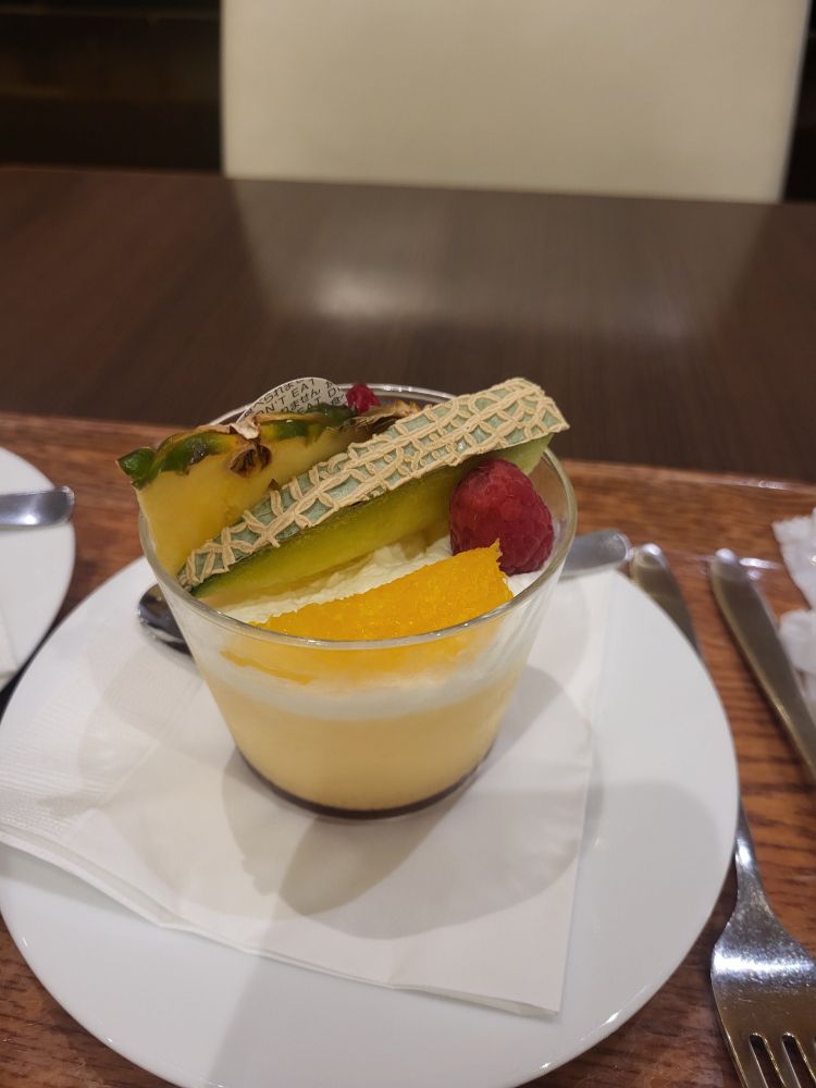 A cup of pudding with various fruits on top. The cup sits on a plate, on a tray.