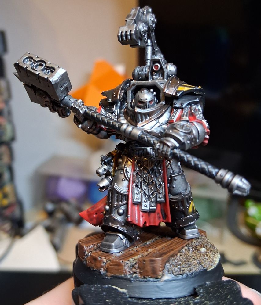 Iron warriors warsmith in cataphractii armour. 

Large armoured man in silver armour with bronze trim, red tabard/cloak/tassets, and a big two handed hammer. He has a mechanical arm mounted over his head