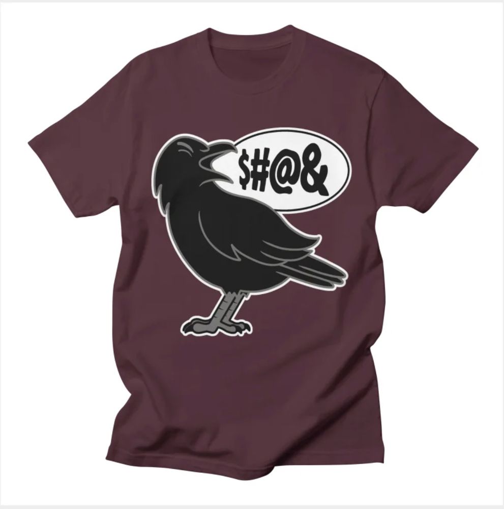 A maroon t-shirt with a black crow cawing loudly. Punctuation marks and other symbols come out of the crow's beak, making it look like it's cursing but in a way that's totally safe for work. Marks used in this way to indicate obscenity are called grawlix. You learned something! Isn't that $#@& cool?