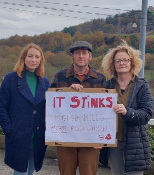Wainhouse Green activists Roseanne and Rachele and local resident Ian Pepper pose in front of a handmade sign that reads 'It stinks: higher bills + more pollution!!'