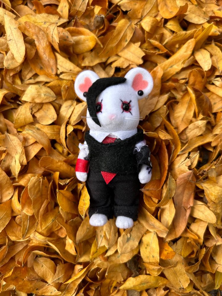 a small mouse figurine dressed like 2005 frank iero laying on a bed of fall leaves